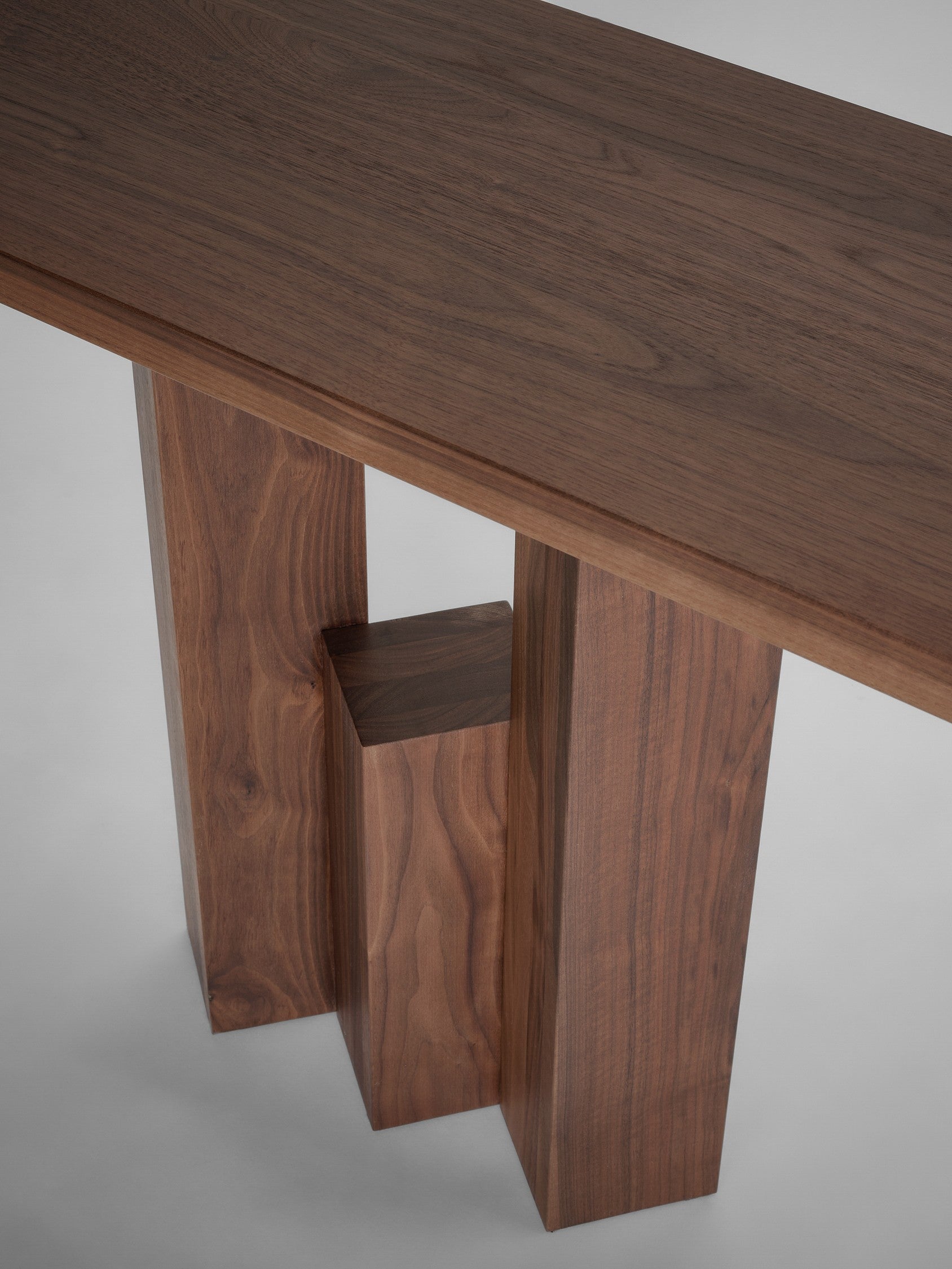 The Fenestra Console by Mokko is a modern wooden table inspired by Brick Expressionism, featuring a thick rectangular top and three block-like legs of varying heights with rich wood grain against a plain background.