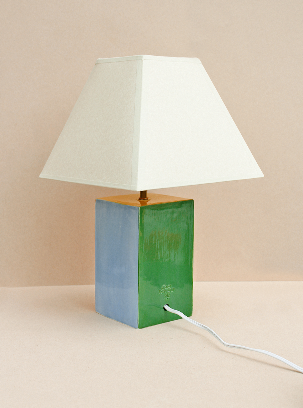 The Paloma Lamp by Casa Veronica features a hand-built ceramic base in two-toned green and blue with a square white custom lampshade and a visible white cord, set against a neutral beige background.