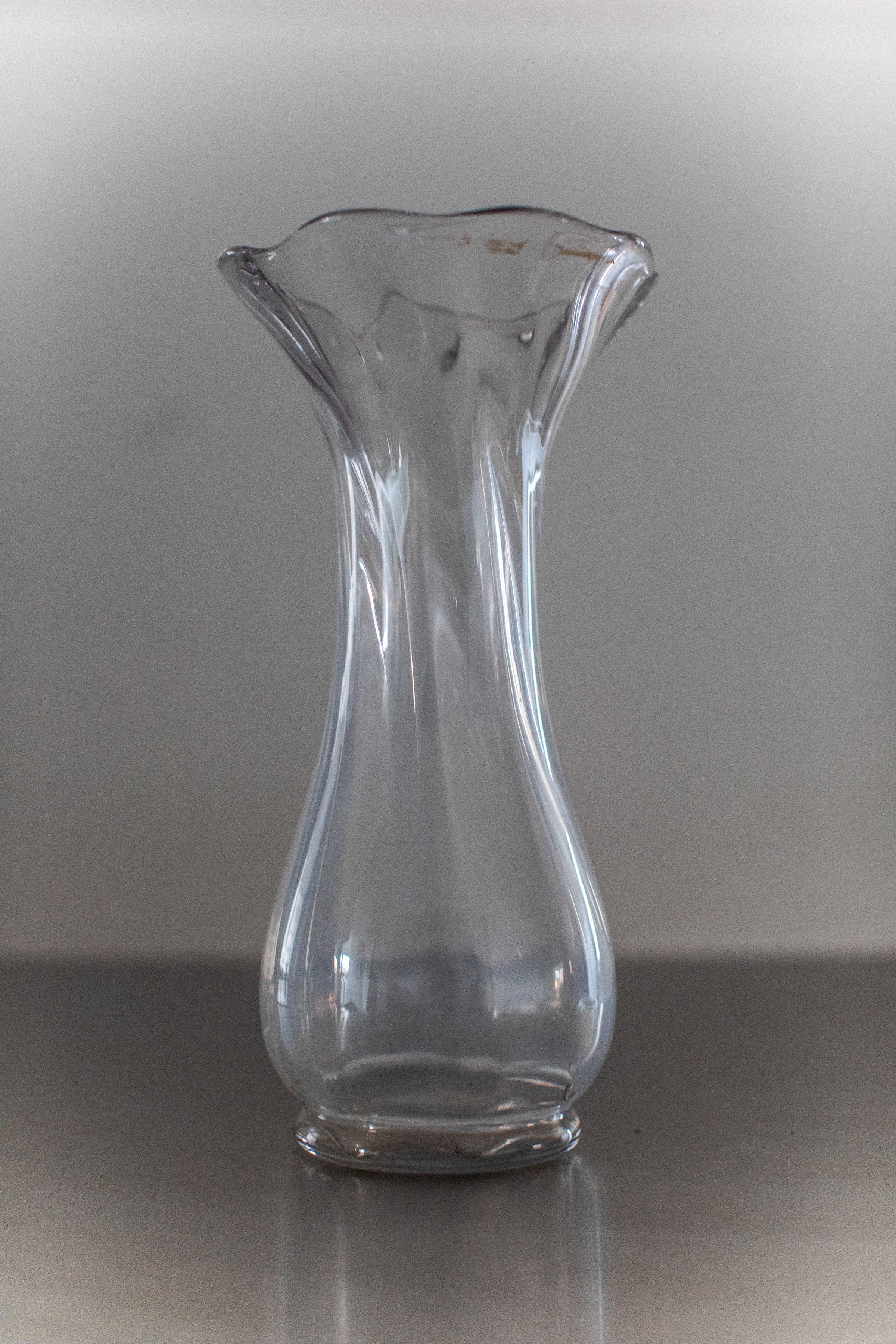 Glass Vase — clear glass with flared top on metal surface