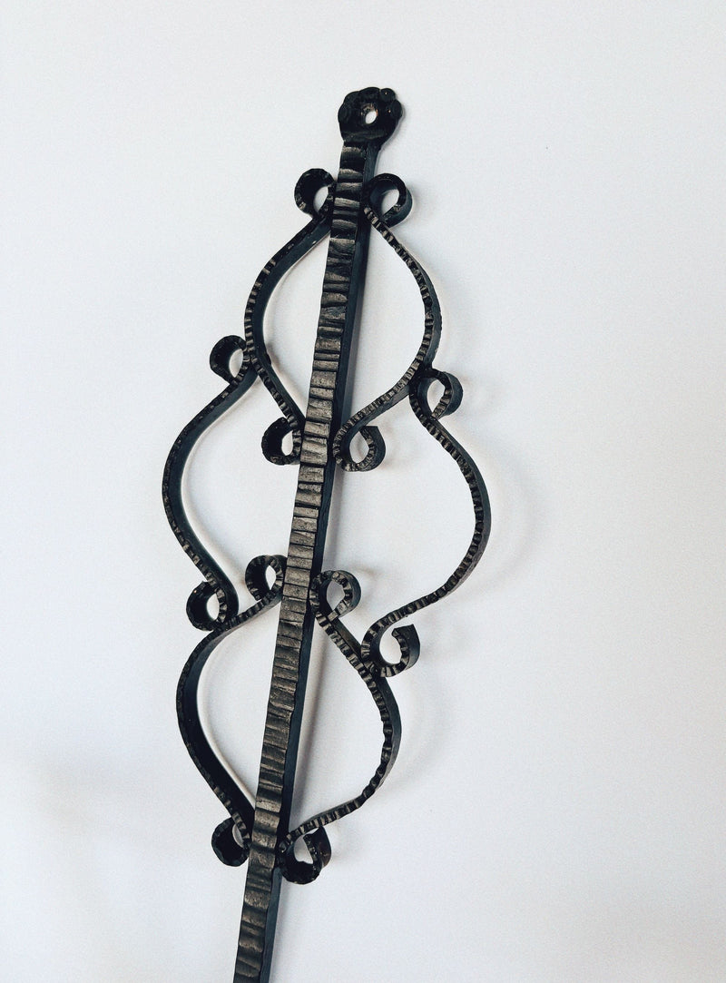 The Huerto Metalwork Wall Candleholder from Poland features a black wrought iron design with a vertical central rod and symmetrical curved scrollwork, displayed against a plain white background.
