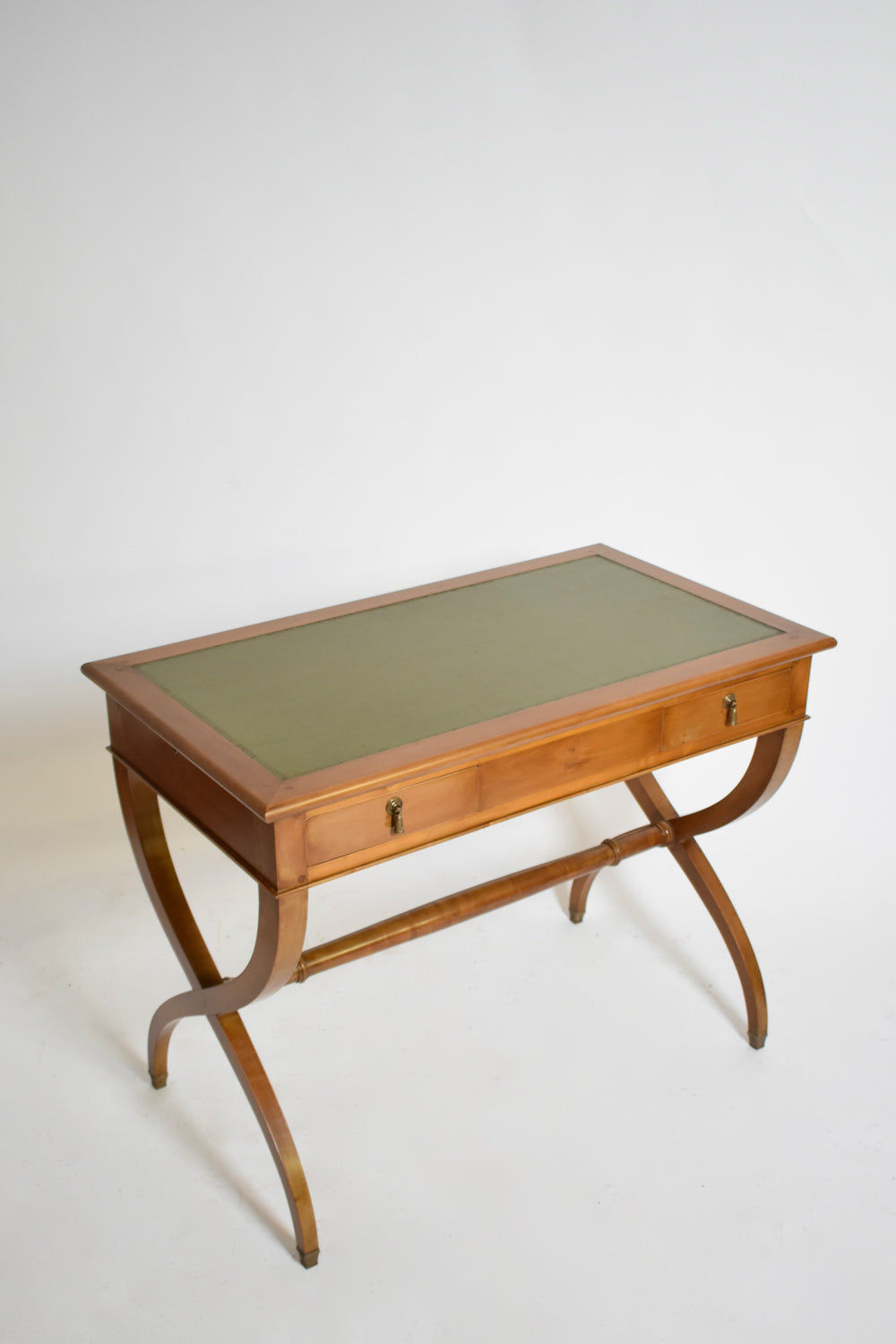 The Barracuda Interiors Directoire style curule console table (1970s) features a wooden frame, green leather or fabric inlay, two drawers with keyholes, and X-shaped curved legs joined by a support bar. Shown on a plain white background.