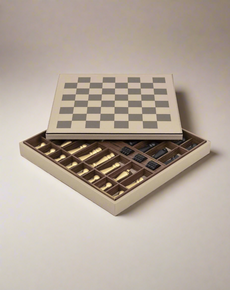 An open wooden Pinetti chess set displaying a game board with chess pieces neatly arranged in an interior storage tray underneath. The pieces are metallic, featuring a mix of gold and silver colors.