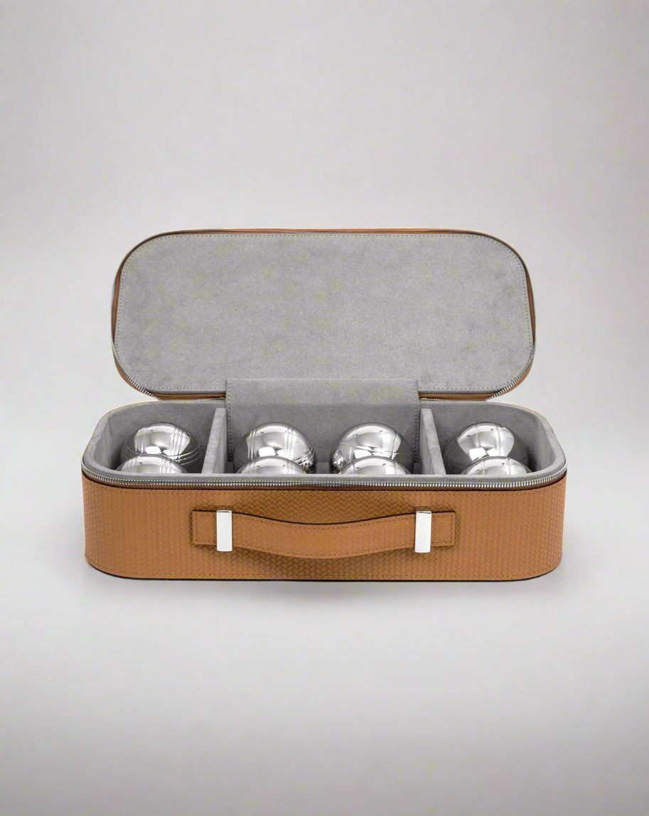 A Pinetti Bowls Game Set, consisting of silver pétanque balls neatly packed inside an open, rectangular tan carry case with a gray interior, isolated on a white background.