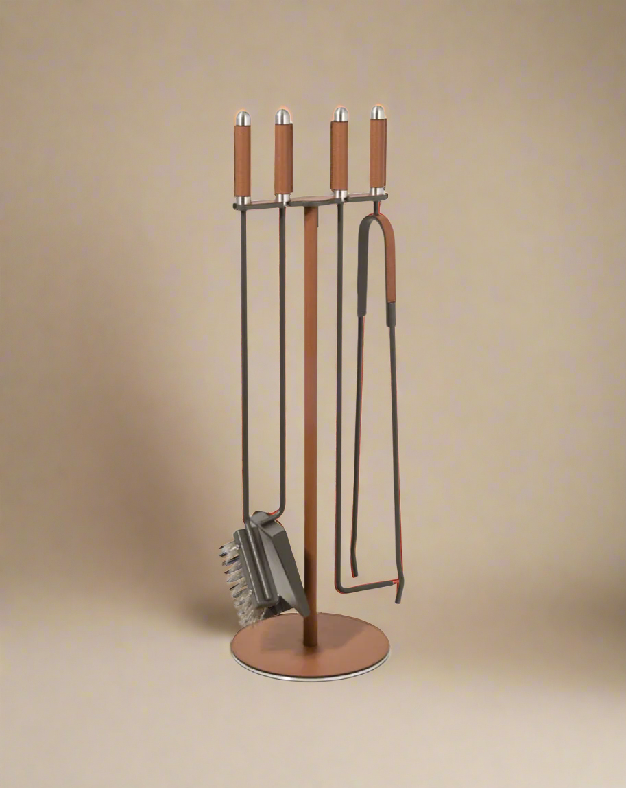 A brown metal Pinetti fireplace set, including a poker, brush, shovel, and tongs with high-quality leather handles, standing on a round base.