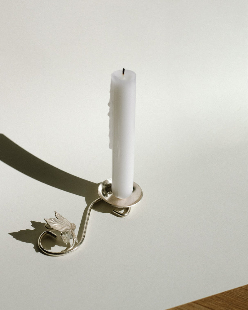 Silver-plated candle holder with decorative leaf detail casting shadow