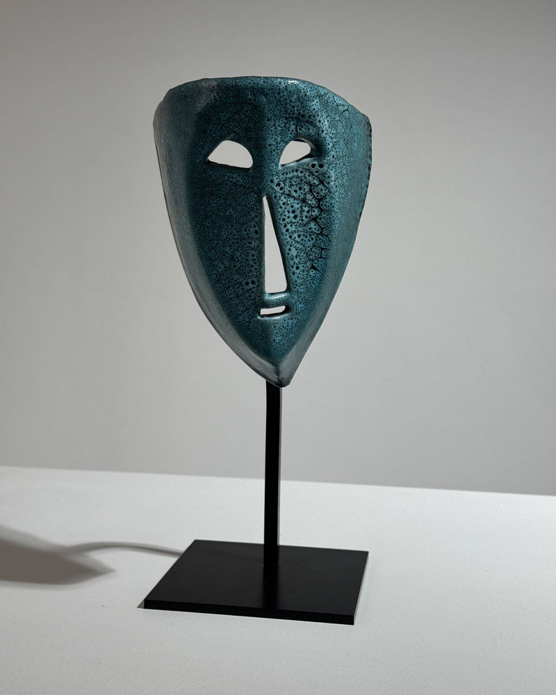 Tribal ceramic mask on black stand showing textured surface detail