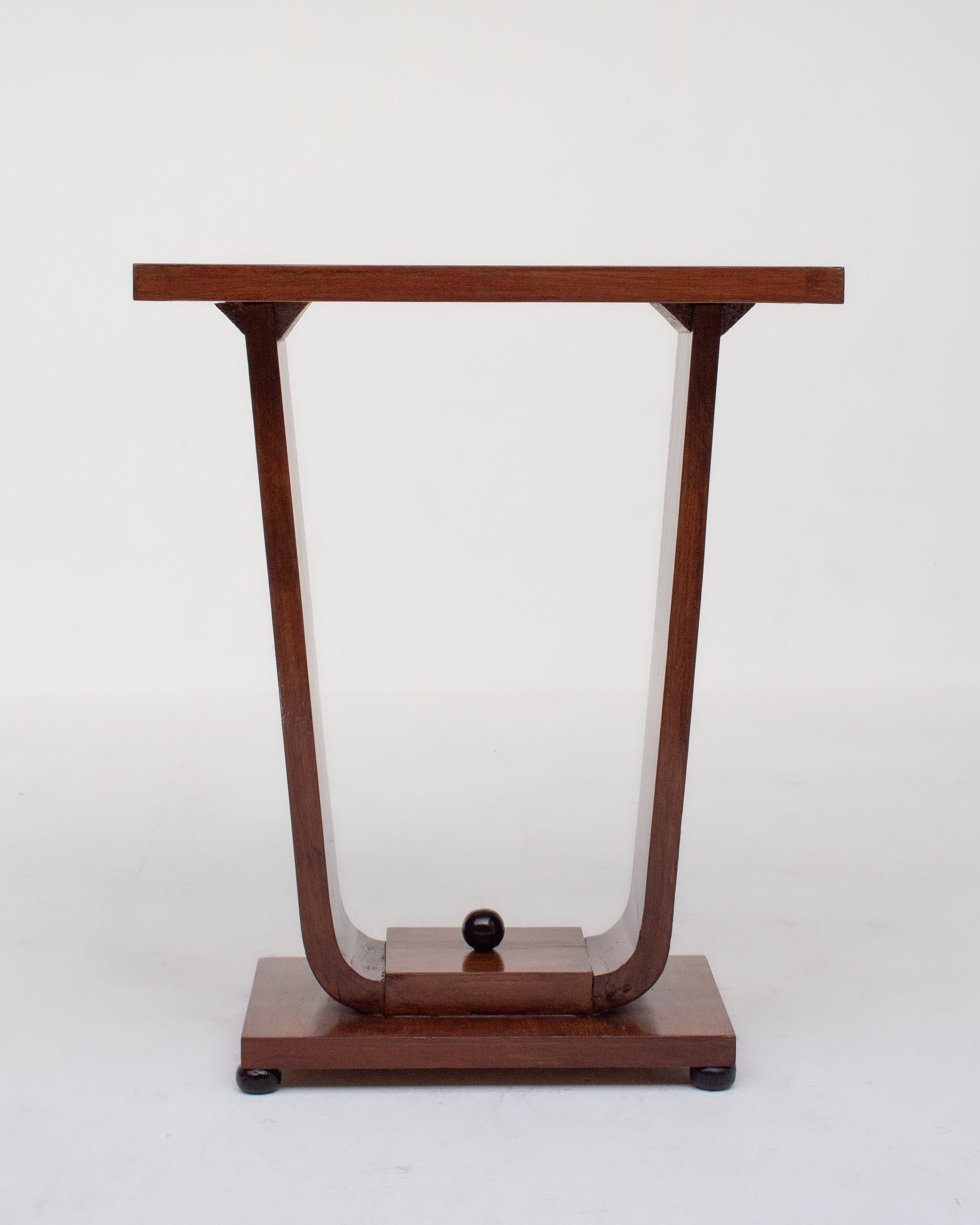 The Malata Antwerp Low Art Deco Side Table features a compact dark wood design with a flat rectangular top, curved U-shaped supports, a central wooden sphere at the base, and a bottom platform—all shown against a plain white background.