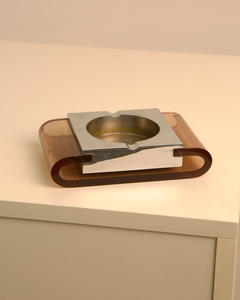 1970s amber plexiglass and metal ashtray on white surface