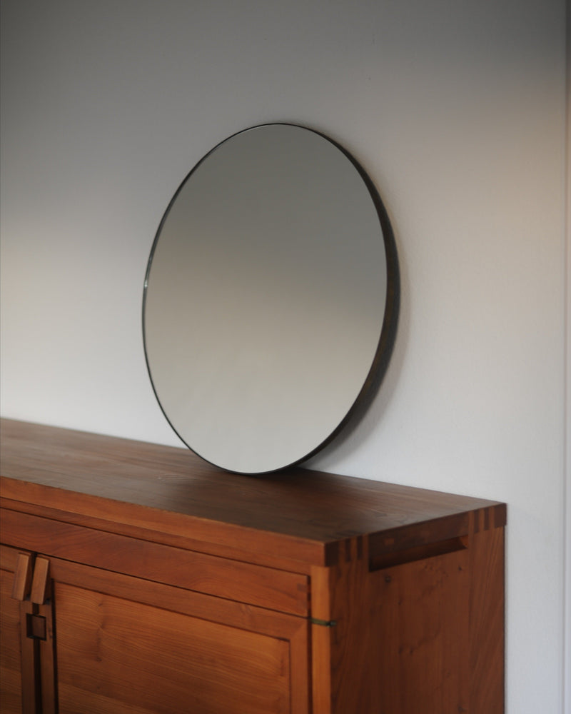 Circular mirror with black frame on mid-century wood sideboard