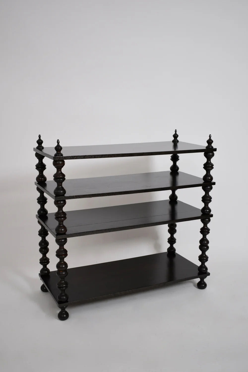 The Barracuda Interiors Ebonised turned wood bookshelves console, 1950s, features four evenly spaced tiers and intricately turned spindle legs, offering classic mid-century style against a plain white background.