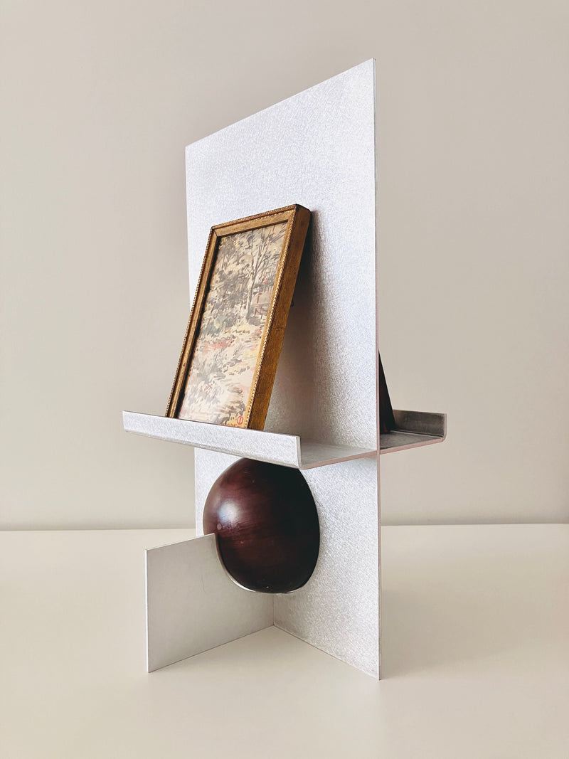 Modern white sculptural easel frame with geometric shelves displaying artwork and ceramic bowl