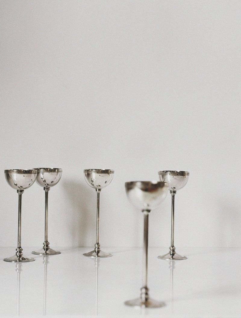 Silver plated coupe glasses with decorative stems on reflective surface