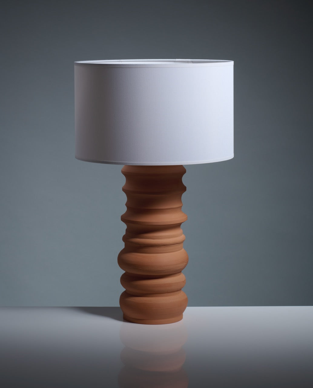 The Katia Langeard Terracotta Glow Table Lamp features a sculpted ceramic base and a large white cylindrical shade, making it an elegant choice for your bedside table arrangement.