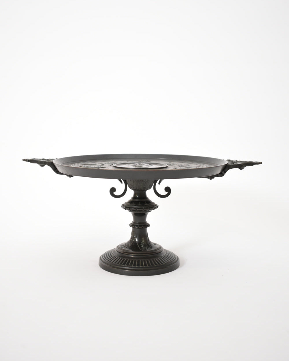 The Barbedienne Style Pedestal Cup, XIXth c. by Barracuda Interiors is a decorative black metal tray with ornate handles and an engraved round surface, styled with an antique patina and displayed against a plain white background.