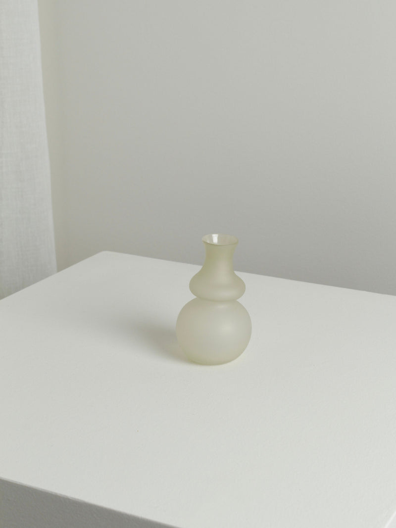 The Small Vase in Stone by Verre d'Onge features a frosted, double-bulb design, adding delicate charm to modern spaces when displayed on a white minimalist surface against a light background.