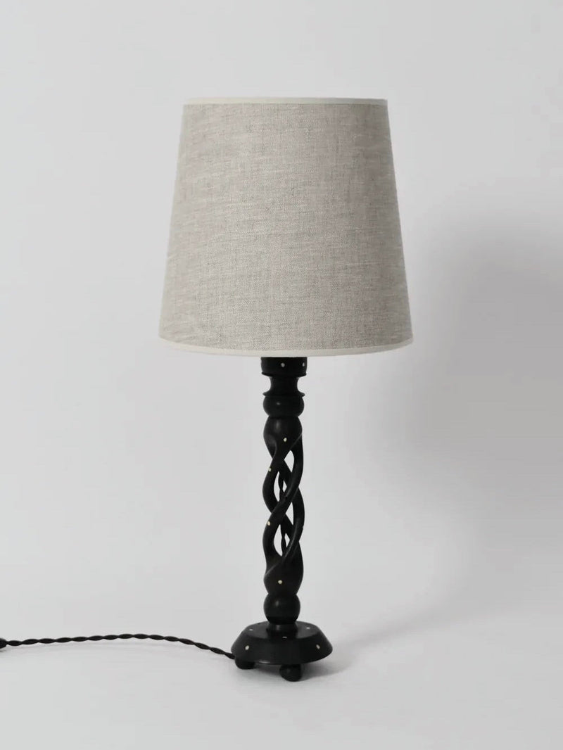 The Turned Wood Twist Lamp by Barracuda Interiors (1960s) features a black twisted base and light beige fabric shade, standing on a white surface with its black power cord extending to the left.