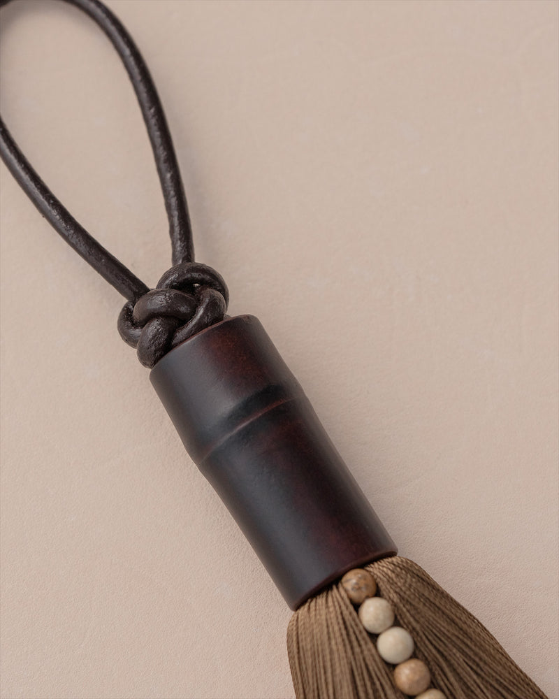 Dark wooden cylinder tassel with beaded cord detail view