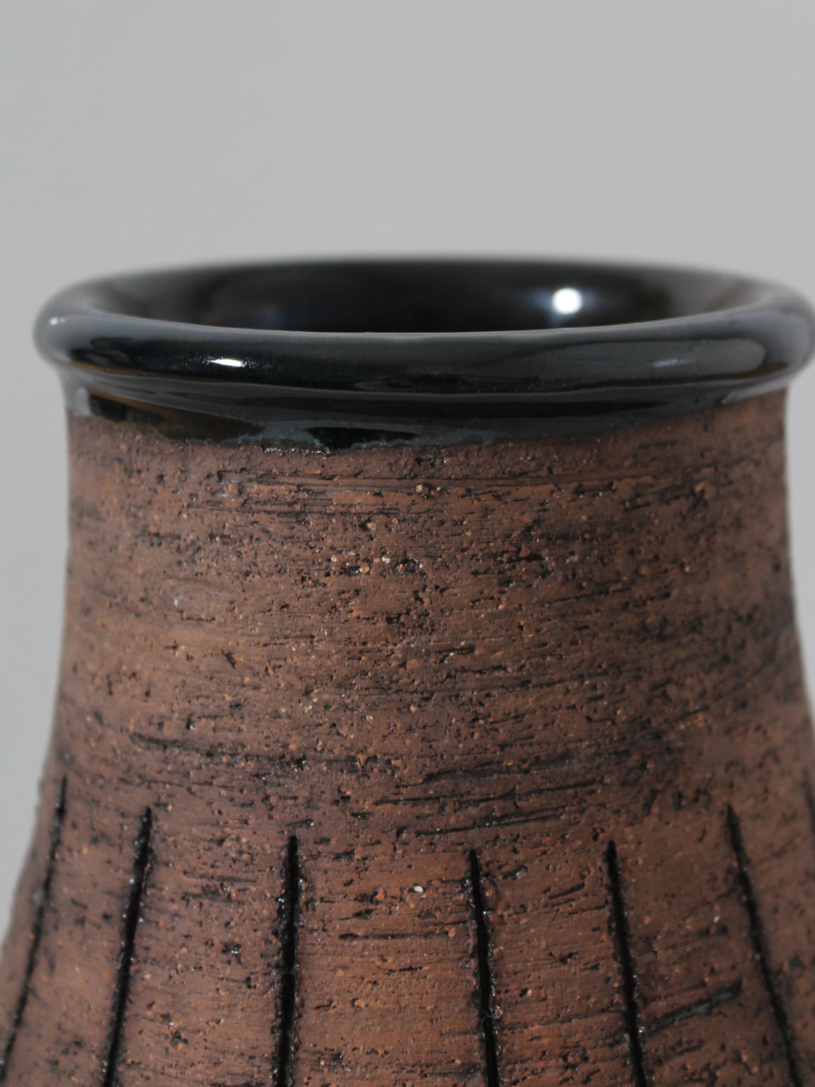 Close-up of the top of an Eke Bjerén Ceramic Vase on Legs for Gabriel Sweden, 1960s by Vintage Stories, featuring a textured grooved surface and glossy black rim, set against a plain light gray background.