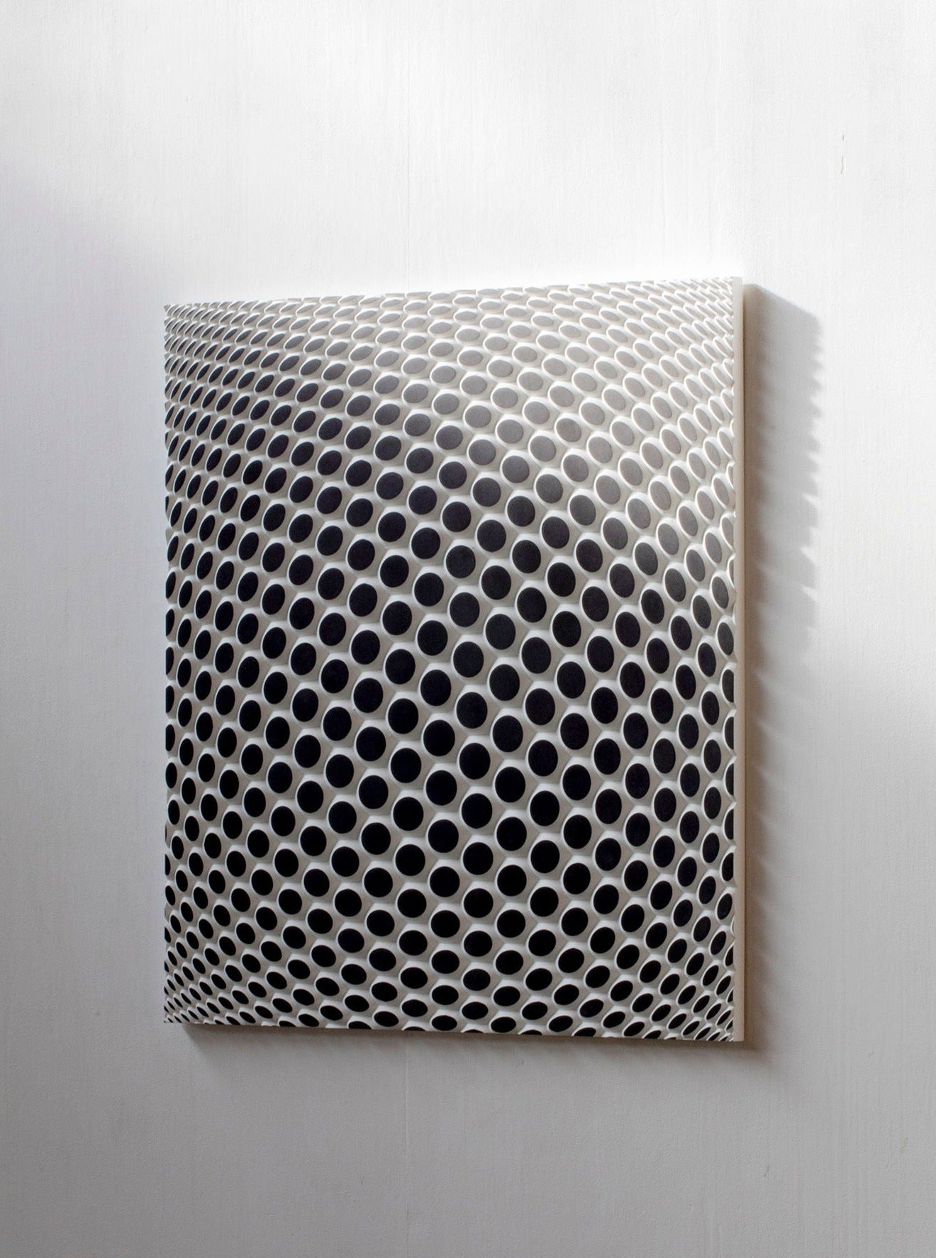 Ommatidium by Studio Arno Hoogland is a square artwork with a grid of raised, ommatidium-like circular holes that form an optical illusion of a 3D bulging sphere on a white background, with shadows adding depth to the effect.