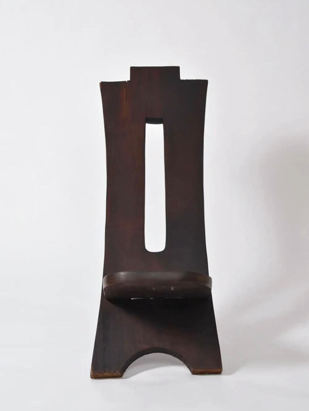 The Barracuda Interiors West African Wood Chair, 1960s, features a tall, narrow backrest with a rectangular cutout and a compact seat near the base. The dark wood chair stands out against a plain white background.