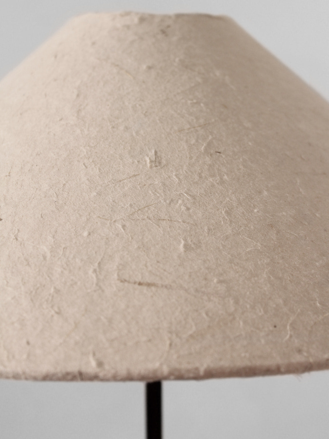 A close-up of the Vintage Stories Mid-Century Swedish Wood And Iron Tall Lamp, showcasing its beige, textured paper shade with a minimalist design inspired by vintage Swedish styles, set against a light gray background.