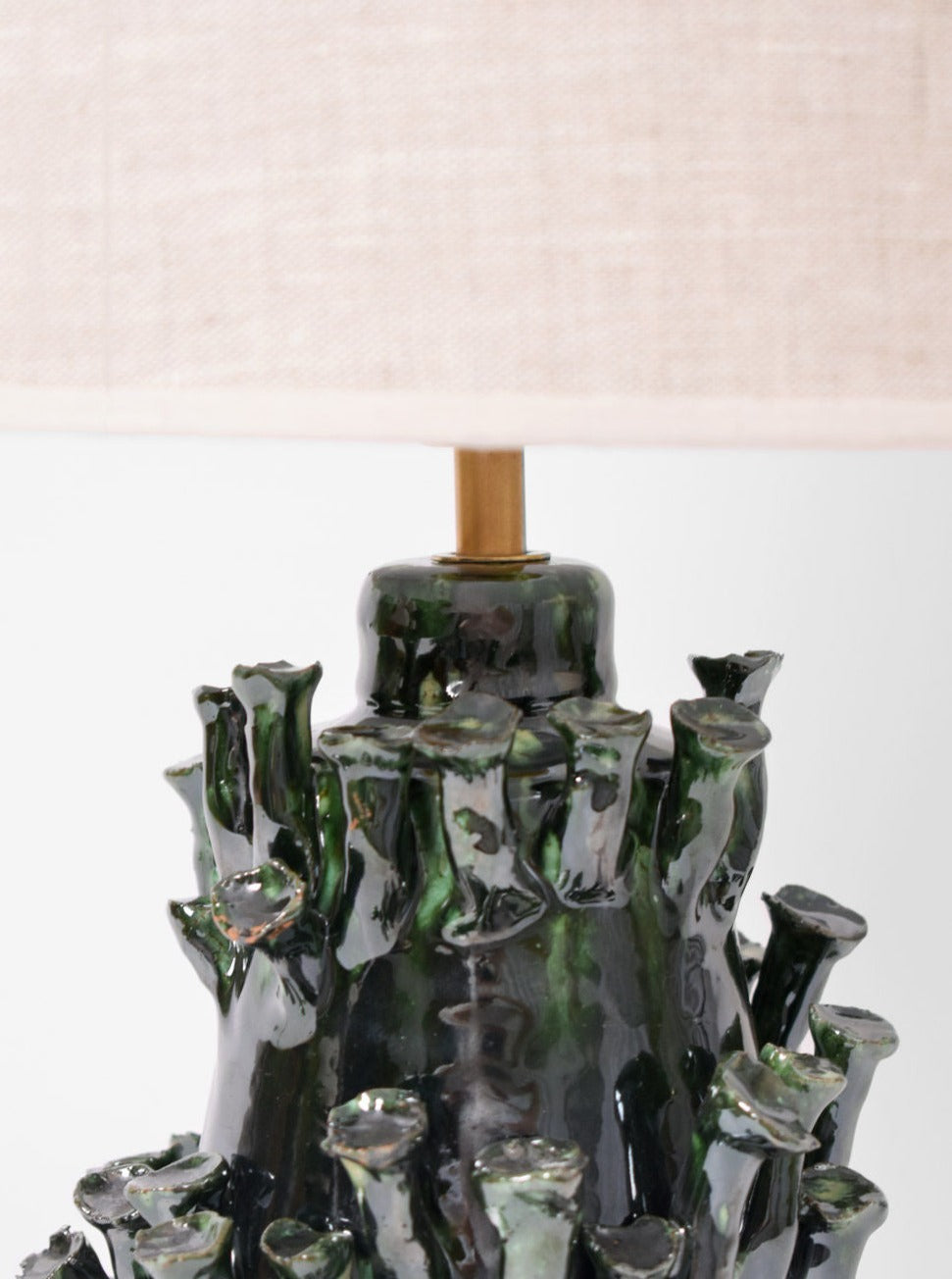 A close-up of the "Belize" Green and Black Lamp by Barracuda Interiors shows its textured, glossy dark green ceramic base with raised shapes and a light beige fabric shade, expertly crafted in Portugal.