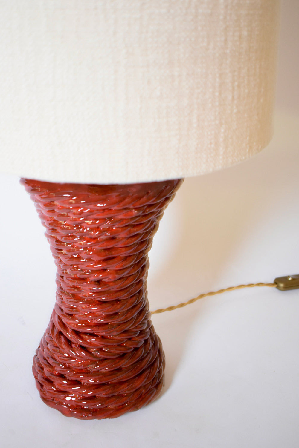The "Kasaï" Red Ceramic Table Lamp by Barracuda Interiors features a glossy, textured red ceramic base with a woven look, a large off-white fabric lampshade, and a braided cord with switch—ideal for bold interior design.