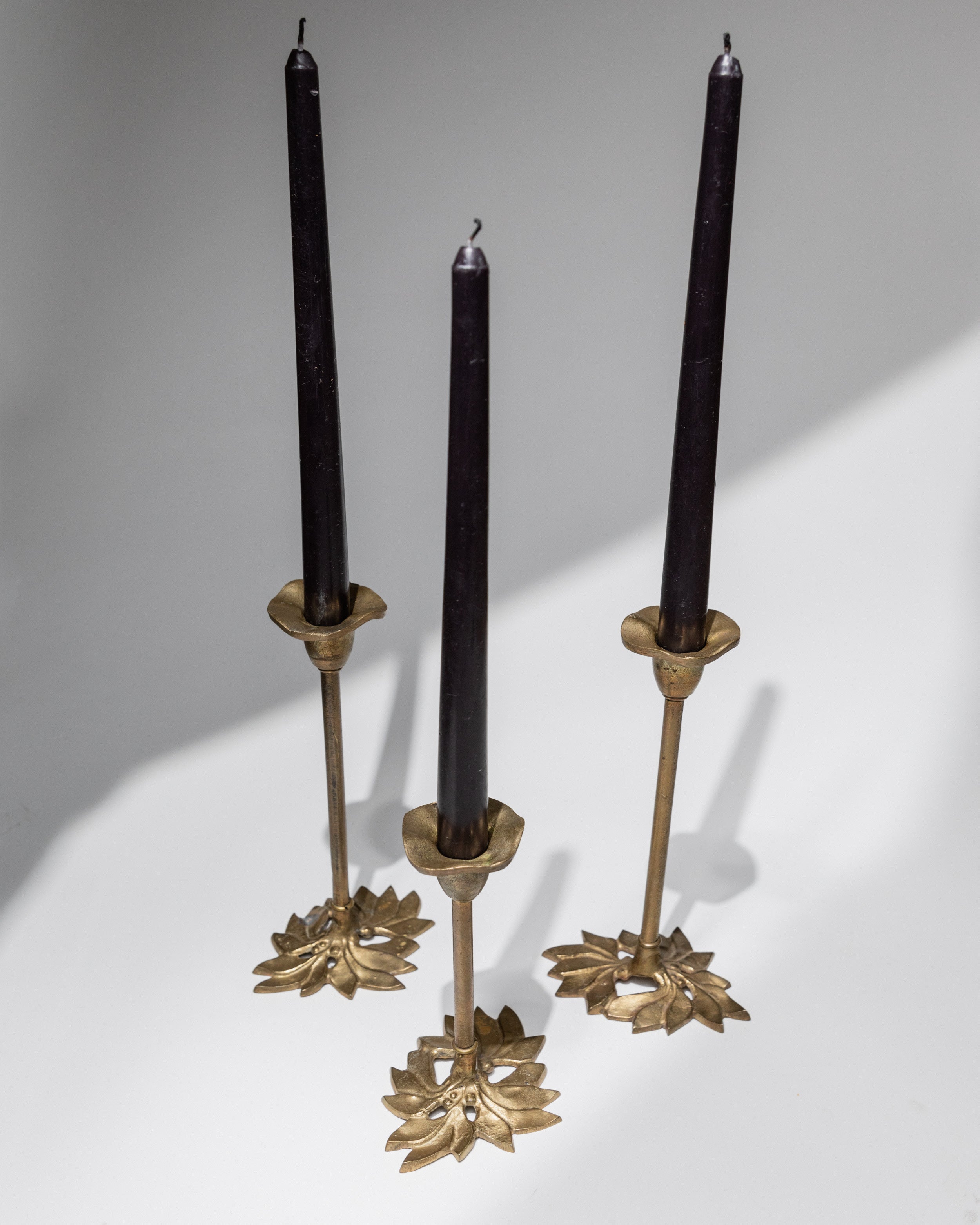 Three brass candle holders with floral bases holding black candles