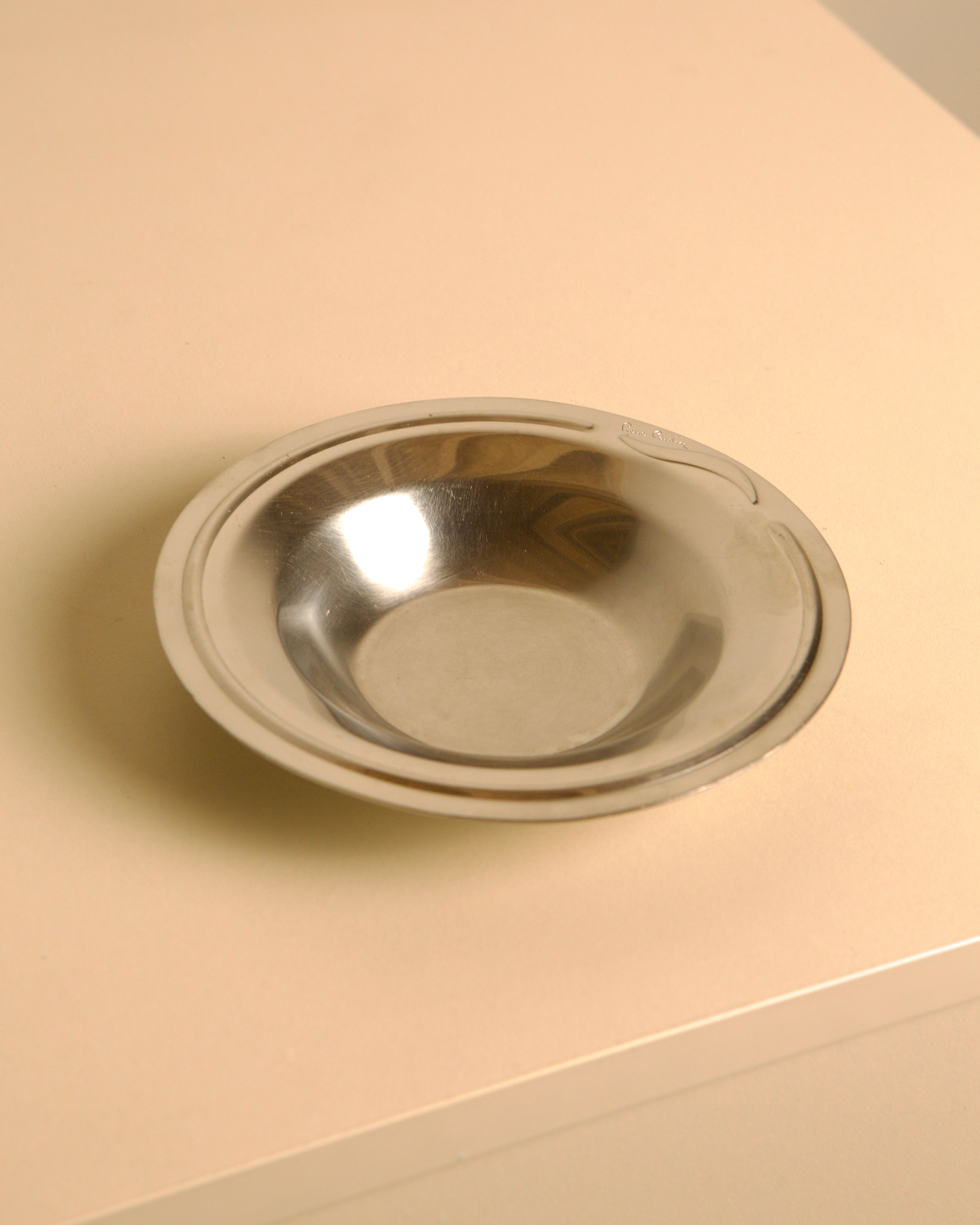 Circular stainless steel valet tray by Pierre Cardin, 1980s — close-up of polished surface on light background