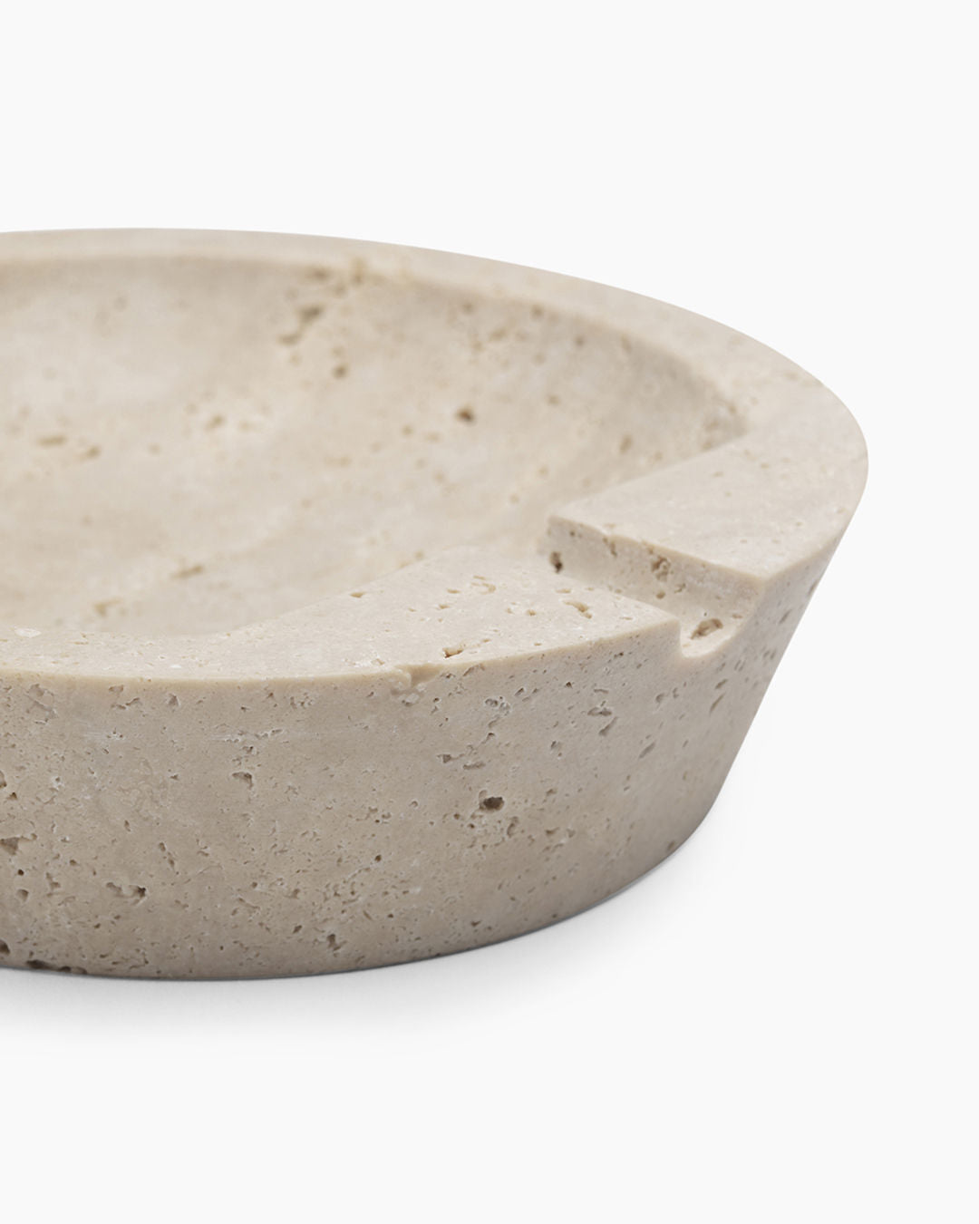 A close-up of the JCL Ashtray in Travertine Stone, featuring a carved notch for holding a cigarette. Its natural, textured, and slightly porous surface gives this piece an elegant yet understated Scandinavian Modern appeal.