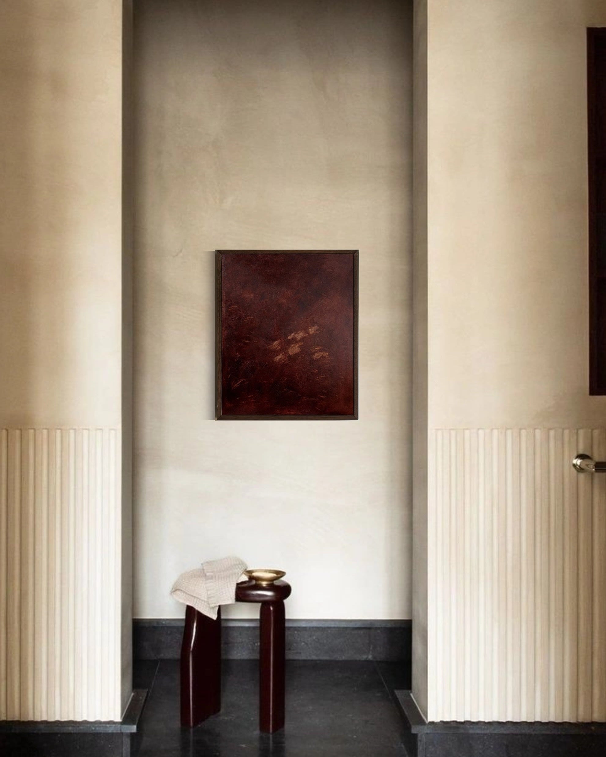 A minimalist hallway features a textured beige wall with vertical grooves, a small dark stool, tray, and folded cloth on a dark floor, accented by Yeliza Gevorgyan’s 'Jane Eyre II' painting in a dark frame.