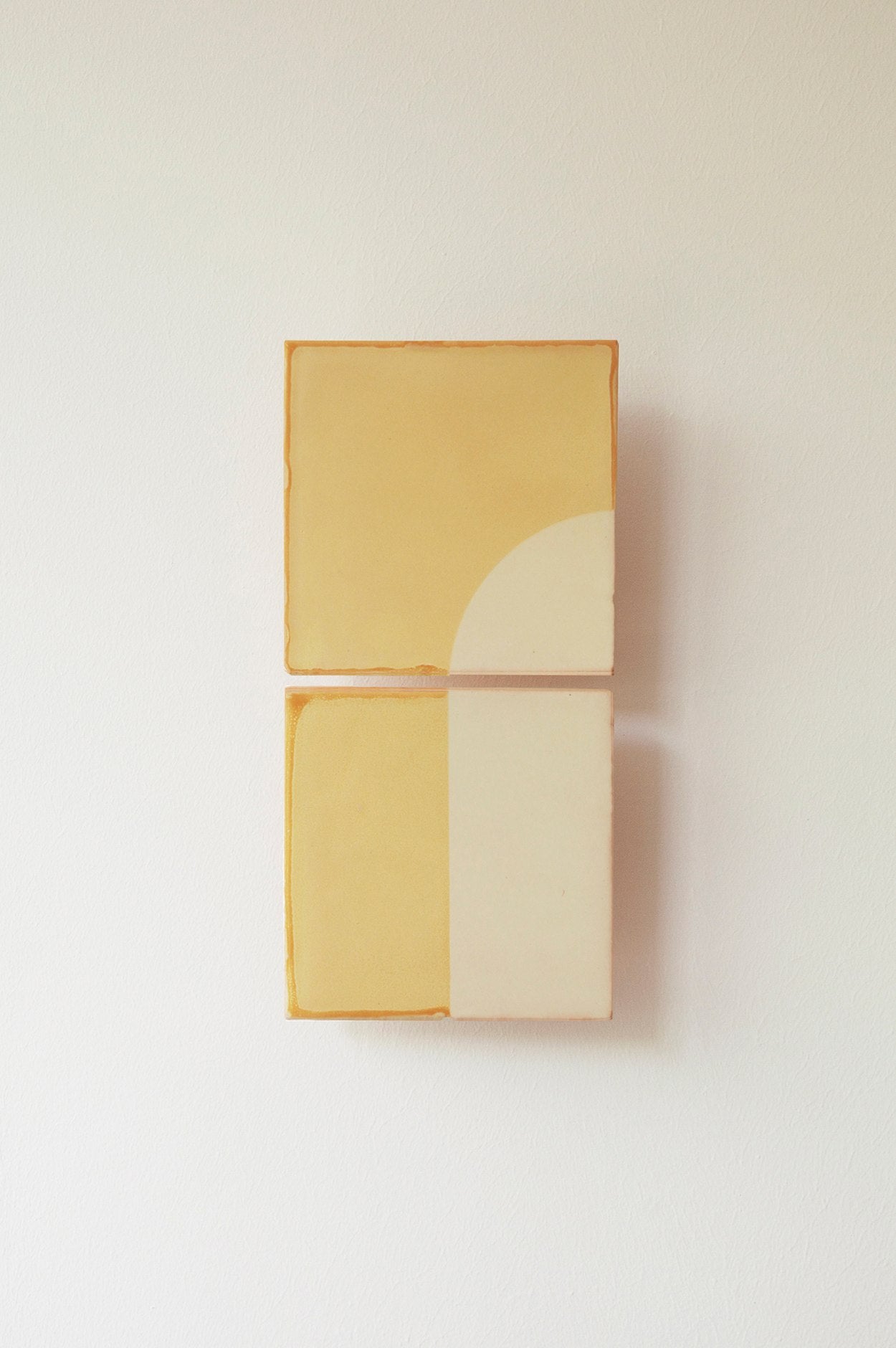 Two rectangular canvases from Violaine d'Harcourt’s "Tiles Door J" feature minimalist geometric forms in muted beige and yellow, with curved and straight lines for a clean, abstract look reminiscent of tiles or a doorway.