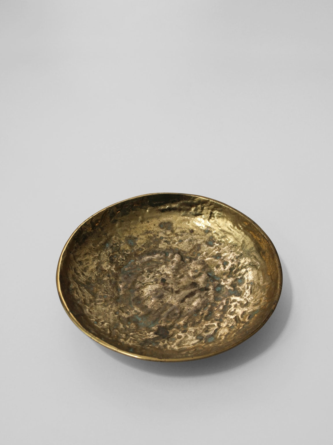 The Massive Organic Textured Brass Bowl by Vintage Stories features a round, shallow hammered brass design with an uneven surface and subtle 1950s vintage appeal, displayed on a plain light gray background.