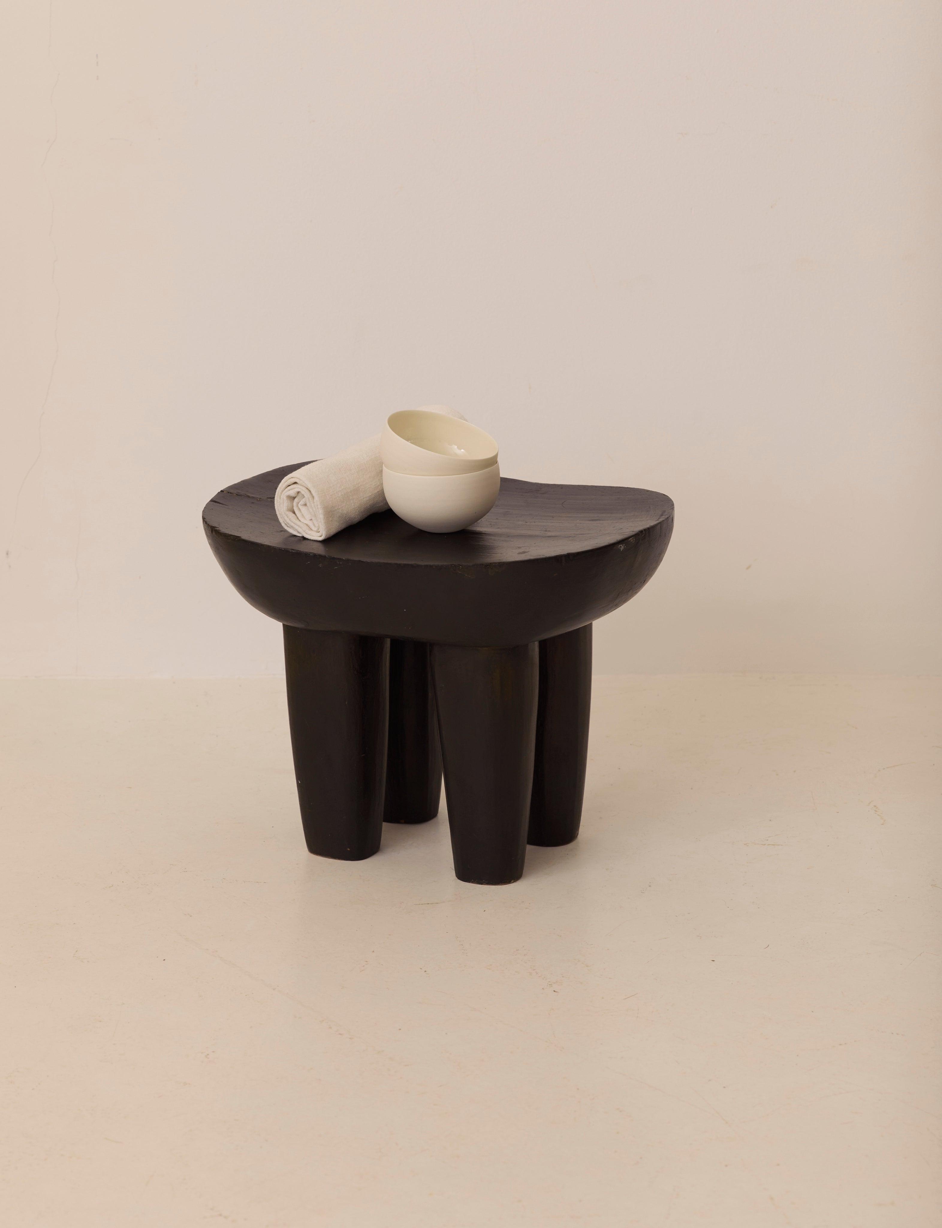 Vintage Senufo Monoxyl African Stool in Black / Wenge — angled view with white towel and bowl