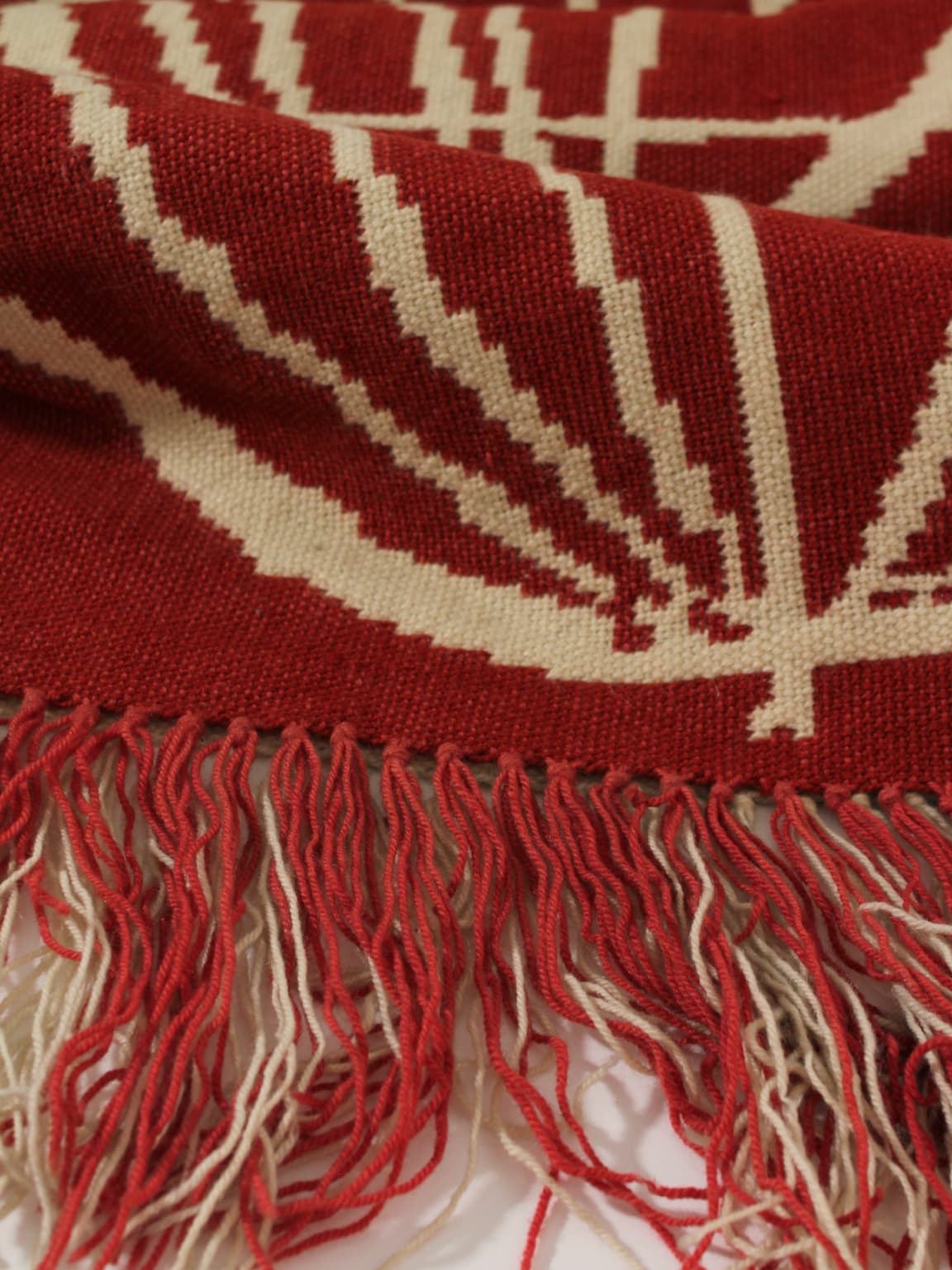 A close-up of the Red Wool Wall Tapestry With Abstract Nature Motifs (72x180cm) by Vintage Stories features bold red and beige designs and textured fringed edges, showcasing detailed craftsmanship in this unique textile art piece.