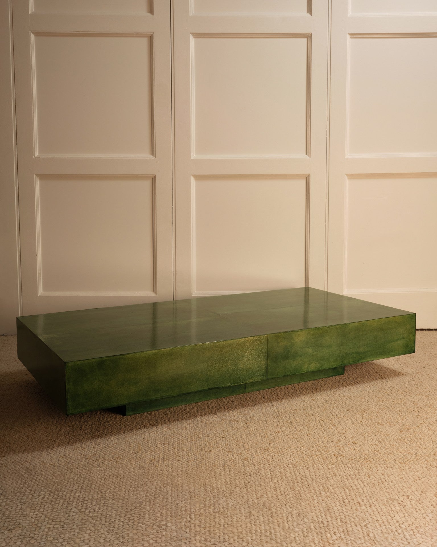The Green parchment table by Galerie Vauvart, featuring a glossy green finish and rectangular shape, rests on a beige carpet before a white paneled wall.
