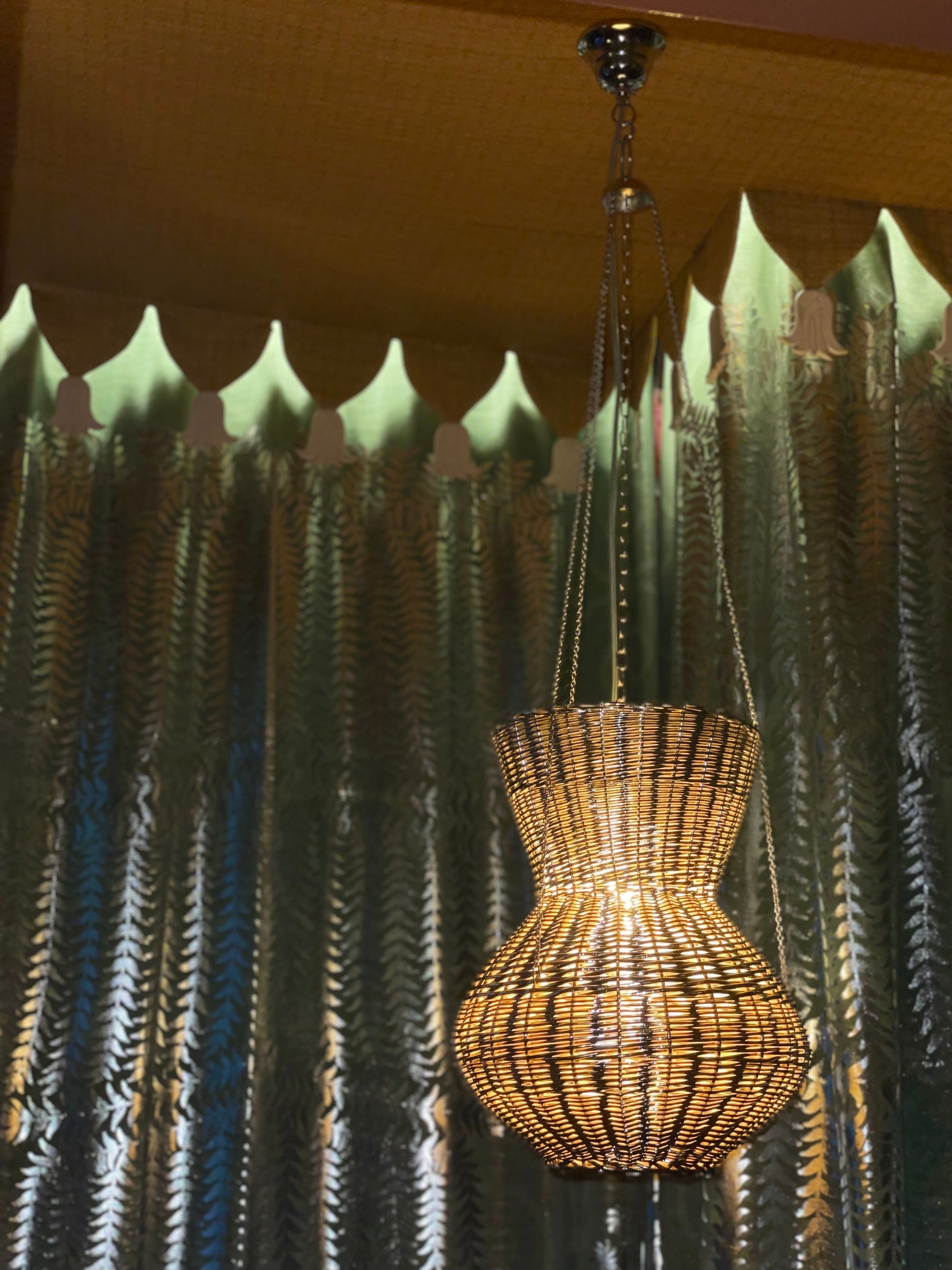 OMAN Contemporary Pendant Light design by Léa Zeroil in Metal and Woven Wicker — hanging in a cozy room with patterned curtai