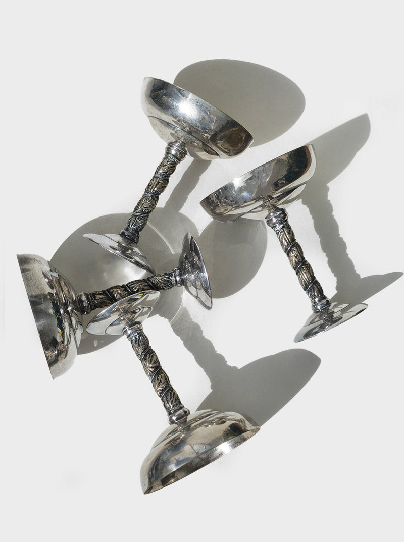 Four ornate silver serving cups with decorative stems arranged artistically