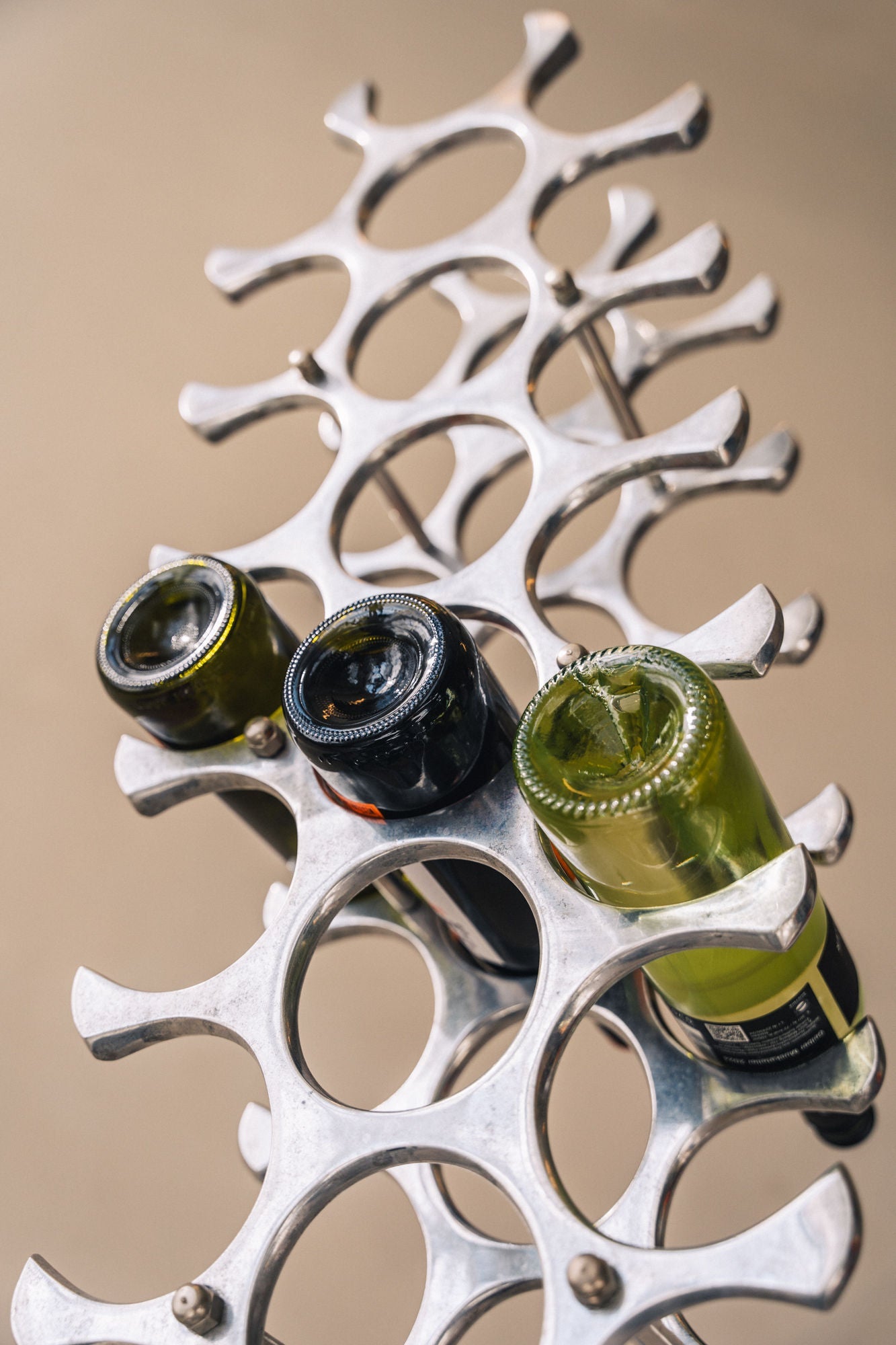 Modern silver wine rack holding green and dark bottles - detail view