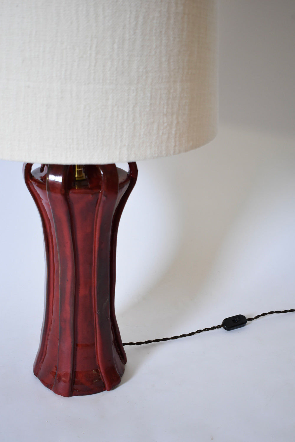 The "Kasaï" Henry Red Ceramic Lamp by Barracuda Interiors features a glossy dark red base, textured off-white shade, and visible black twisted cord with inline switch, set against a white background.