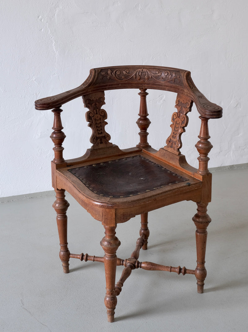 Ornate carved wooden corner chair with black leather seat detail