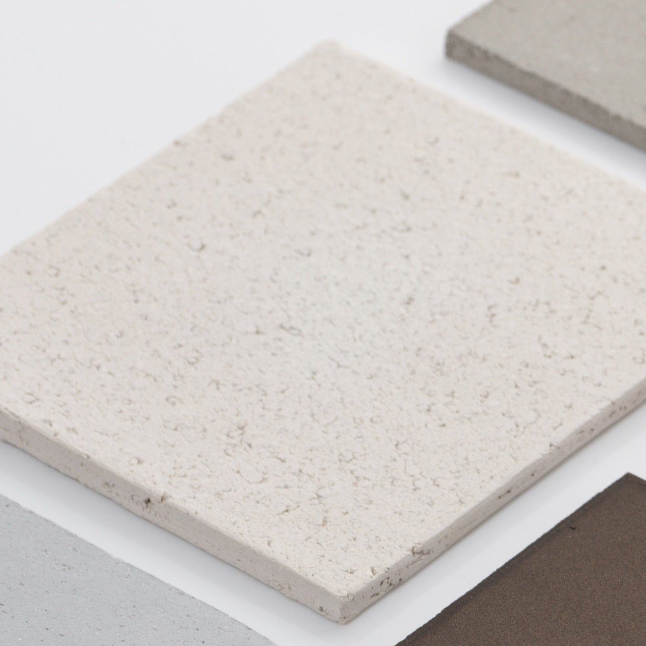 A close-up of four square ceramic tiles in white, light gray, beige, and brown on a white background—ideal inspiration for styling your space with the "Bricks" Table Lamps in Ceramic by Katia Langeard.