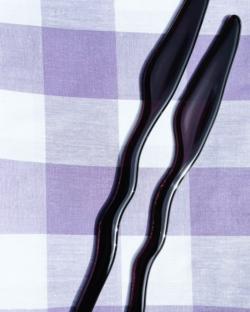 Two curved black Memphis butter knives on checkered tablecloth
