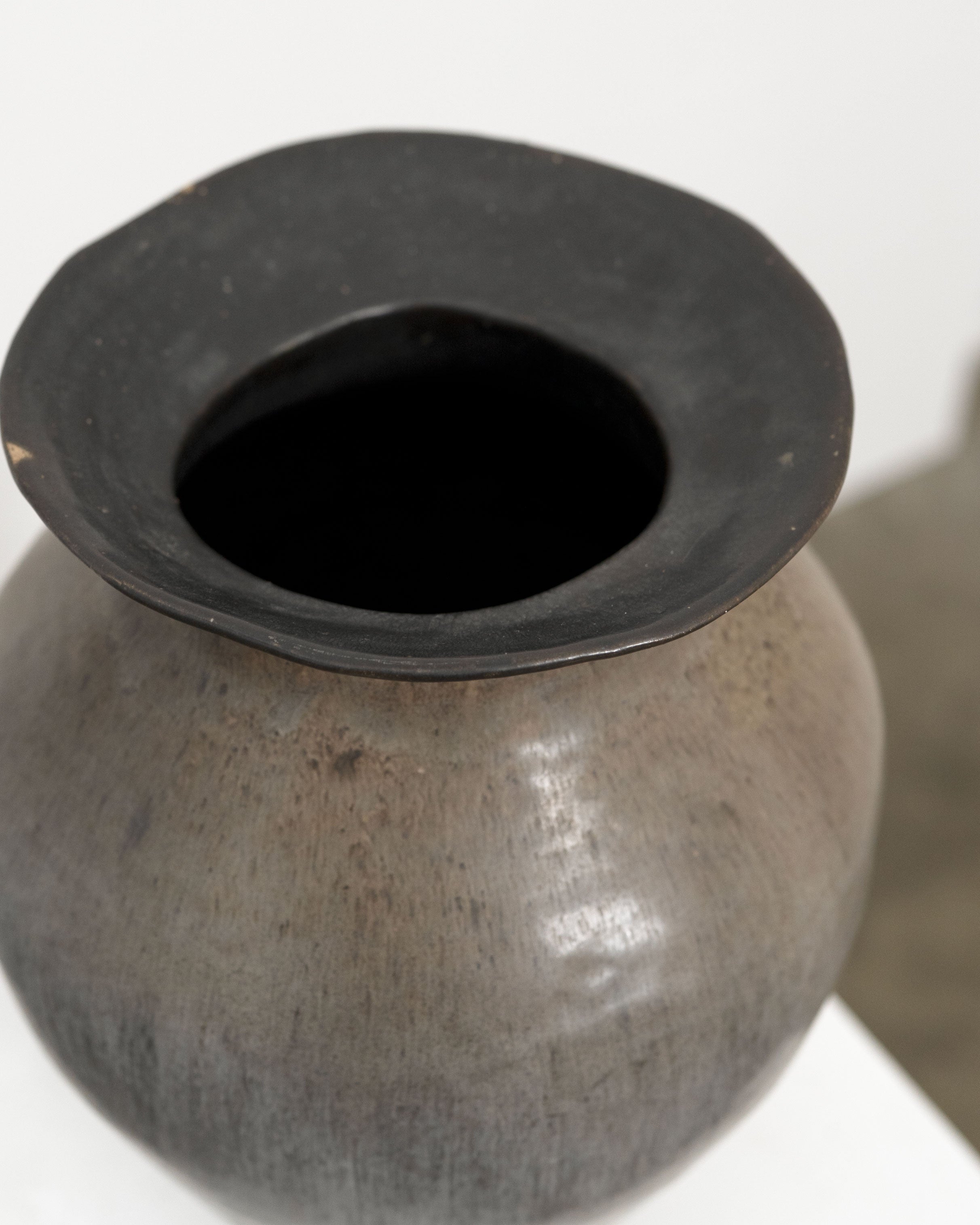 A close-up of the Hand Built Studio Pottery Vase by Tom Bogle, featuring a round shape, dark irregular rim, and smooth mottled stoneware surface—an artisanal piece shown on a white background.