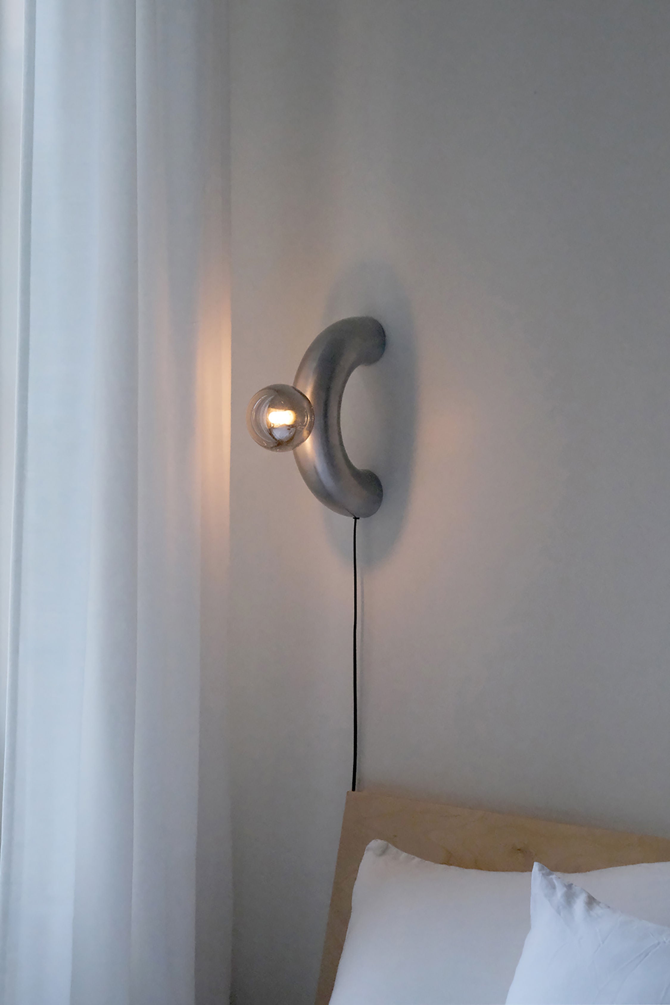 Modern aluminum arc wall lamp with glass globe in minimalist bedroom setting
