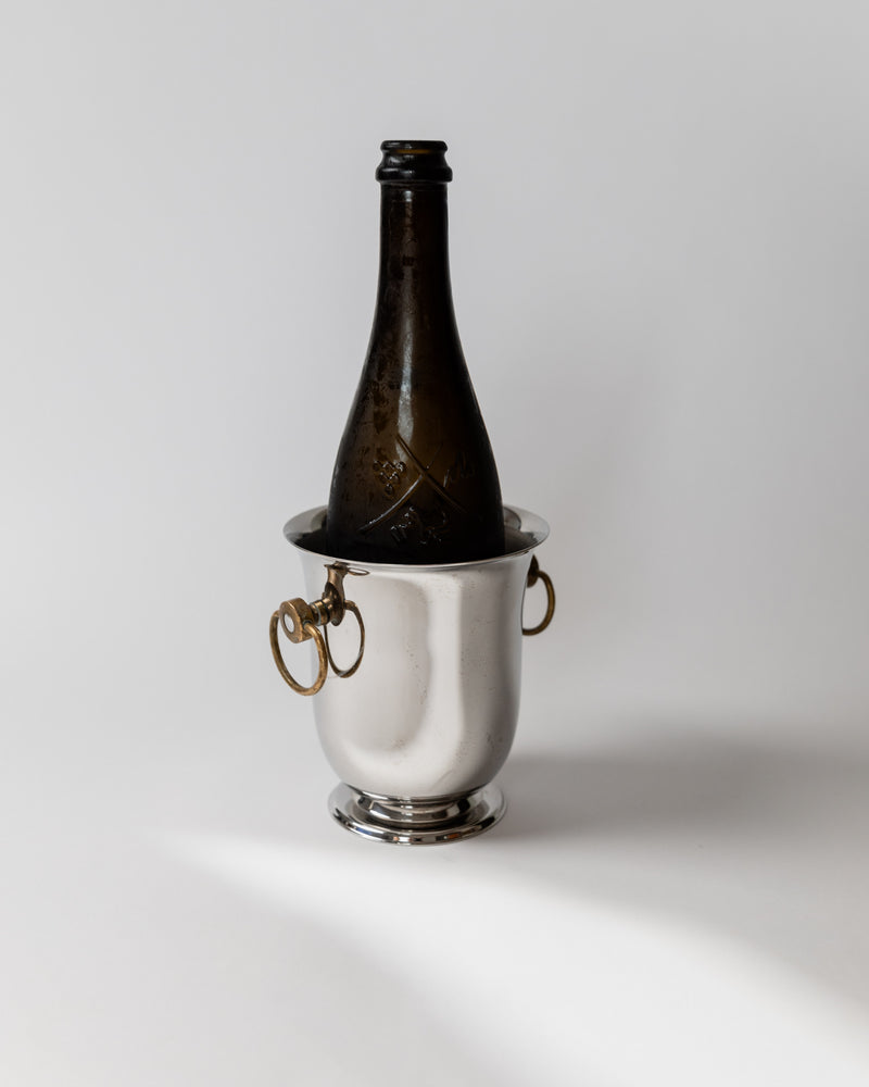 Silver champagne cooler with brass handles and dark bottle