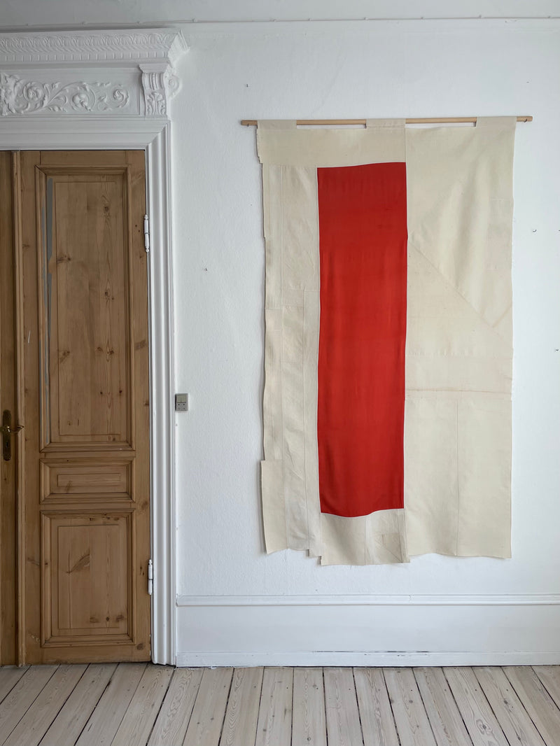 Contemporary textile art with red vertical stripe on cream fabric hanging on white wall