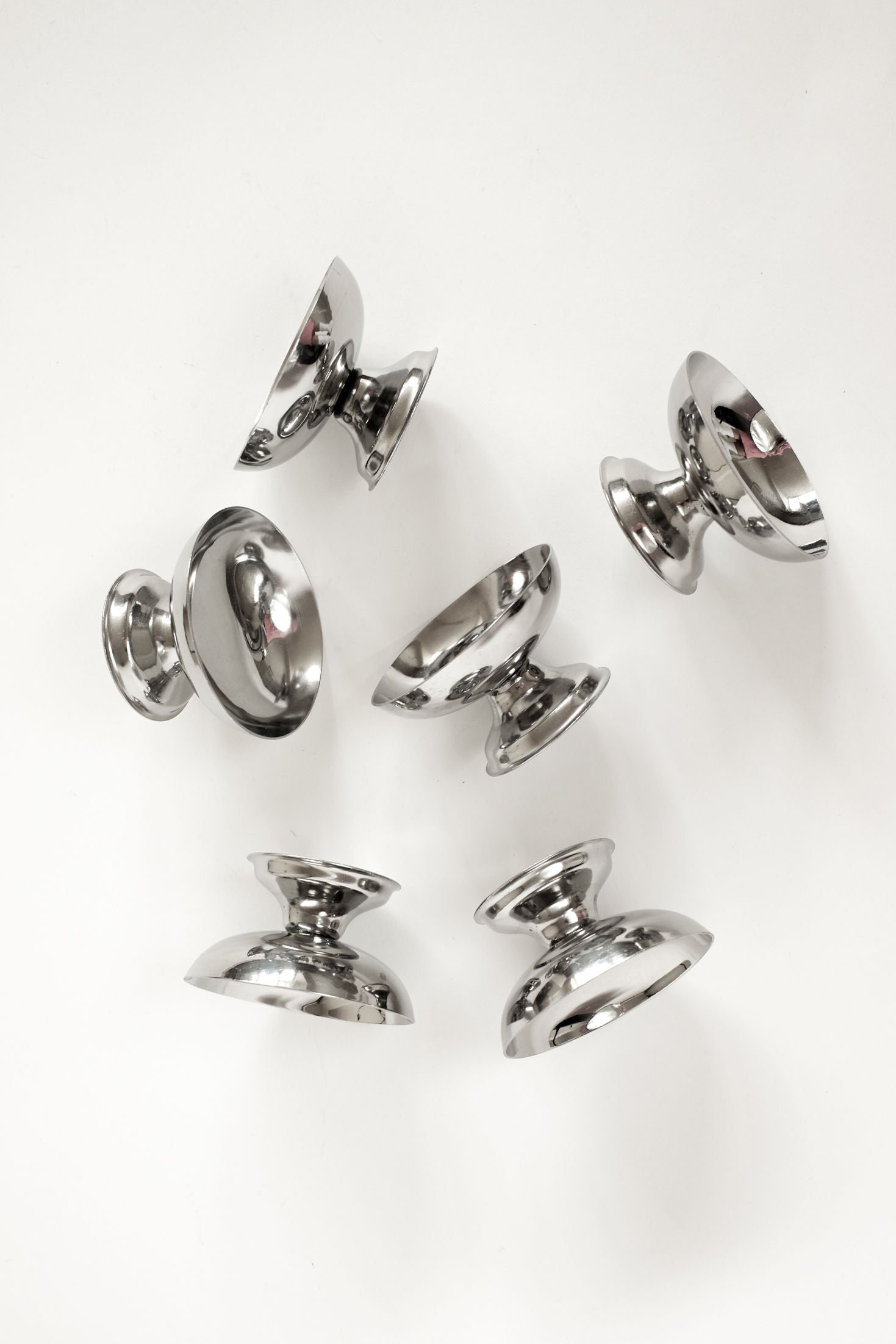 The Set of Six Ice Coupes by septembre studios features shiny, metallic cocktail glasses with flared bases. Arranged on a white background, their reflective surfaces create elegant highlights and mirrored reflections.