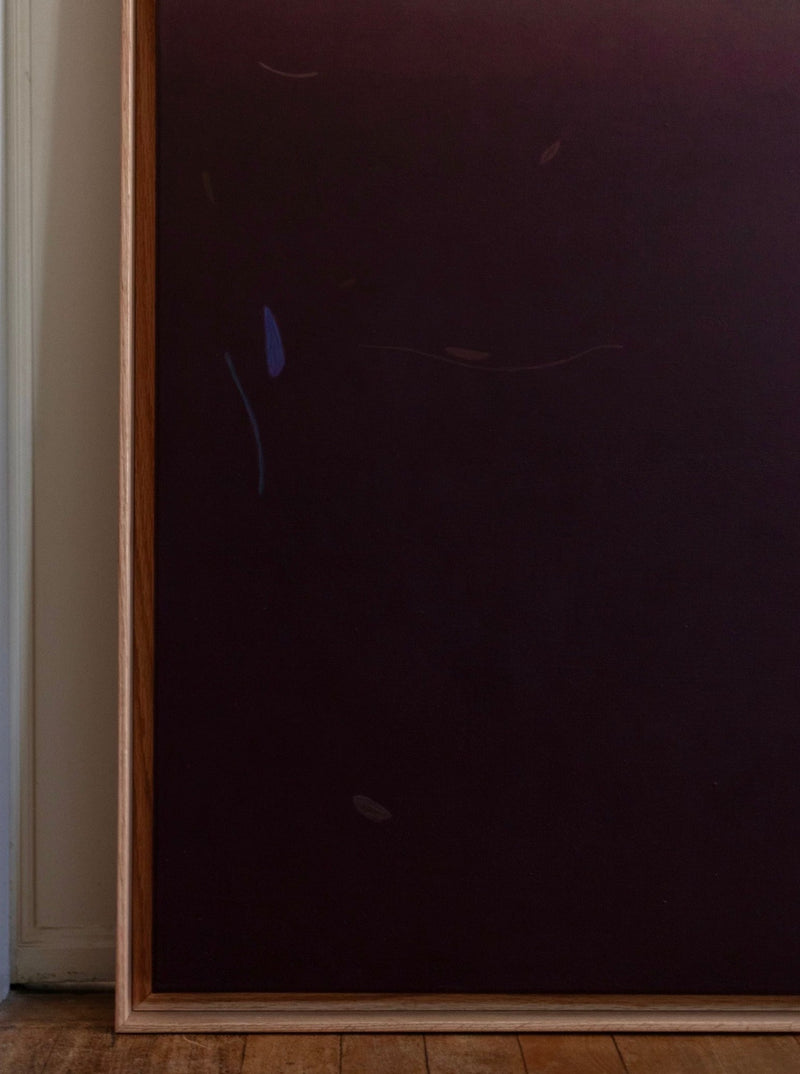 A painting with a hard waxed oak frame leans against a white wall. The artwork features a gradient of dark hues, primarily purples and browns, with subtle abstract shapes and lines. Acrylics on canvas, "Something(s) in the air, 2024" by Rebecca von Matérn rests on a wooden floor.