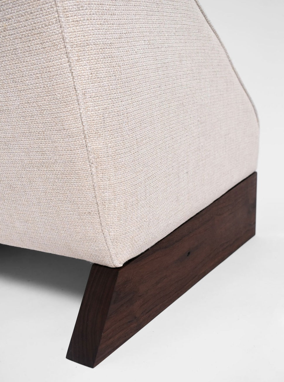 Close-up of the Arrábida Armchair by Barracuda Interiors, featuring light beige textured upholstery and a dark wooden base with a slanted, angular design, set against a plain background.